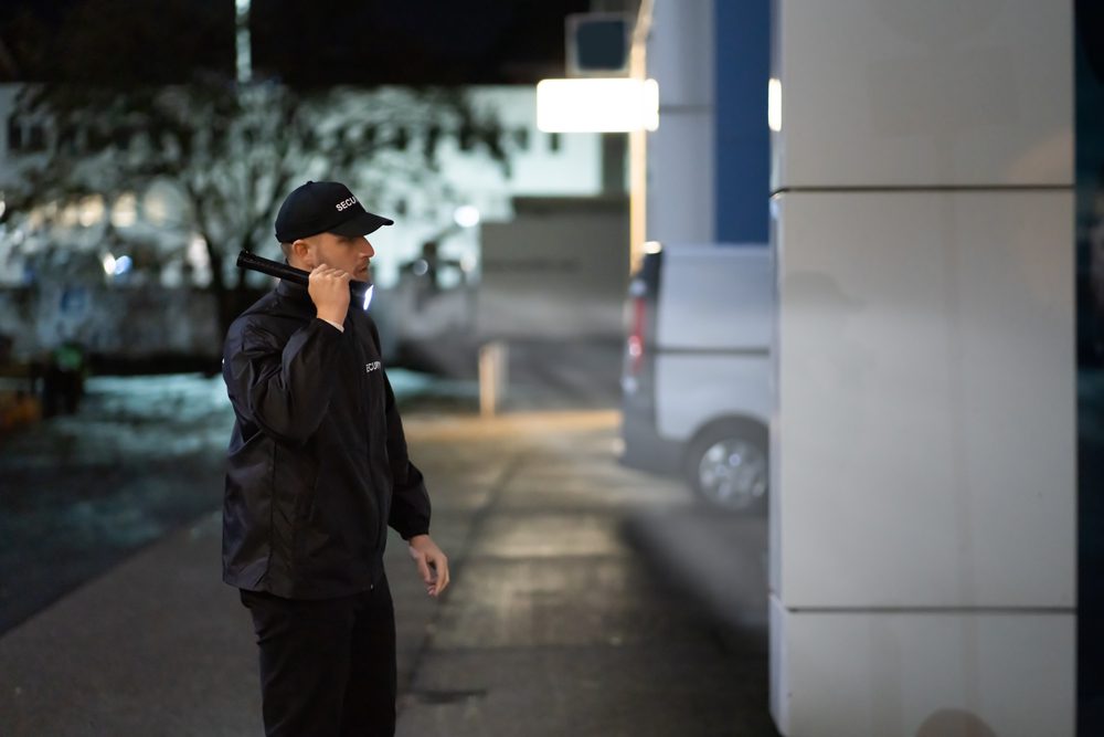 Security,Guard,Walking,Building,Perimeter,With,Flashlight,At,Night