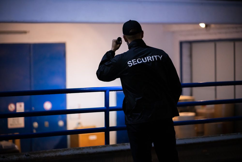 Security,Guard,Walking,Building,Perimeter,With,Flashlight,At,Night