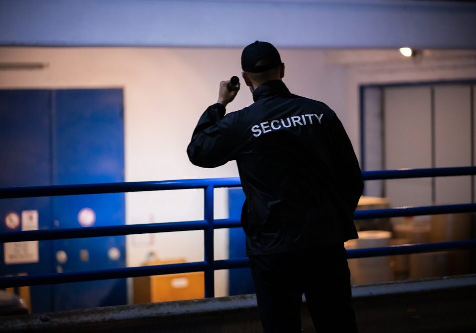 Security,Guard,Walking,Building,Perimeter,With,Flashlight,At,Night