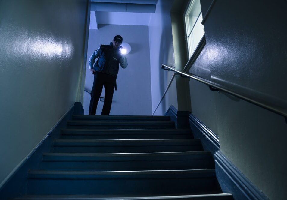 Male,Security,Guard,Searching,On,Stairway,With,Flashlight